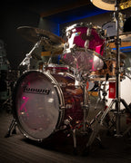 Ludwig Vistalite 3-piece purple drum kit with bass drum, snare, and tom drums, set up on a stage with drumsticks.
