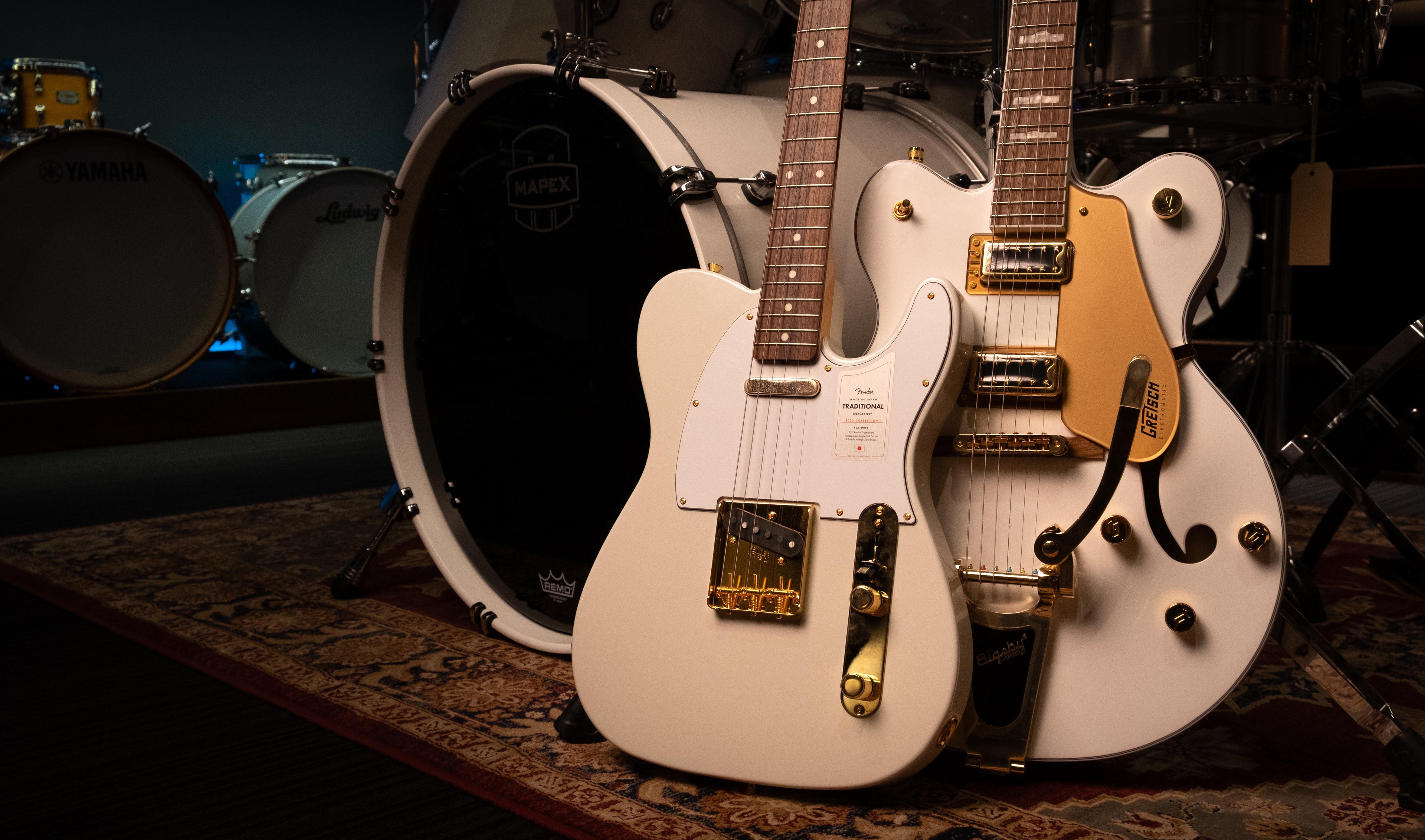 An arrangement of white nusical instruments including a Fender Made in Japan Traditional Telecaster Electric Guitar, a Gretsch Hollowbody Guitar and a Mapex drum kit.