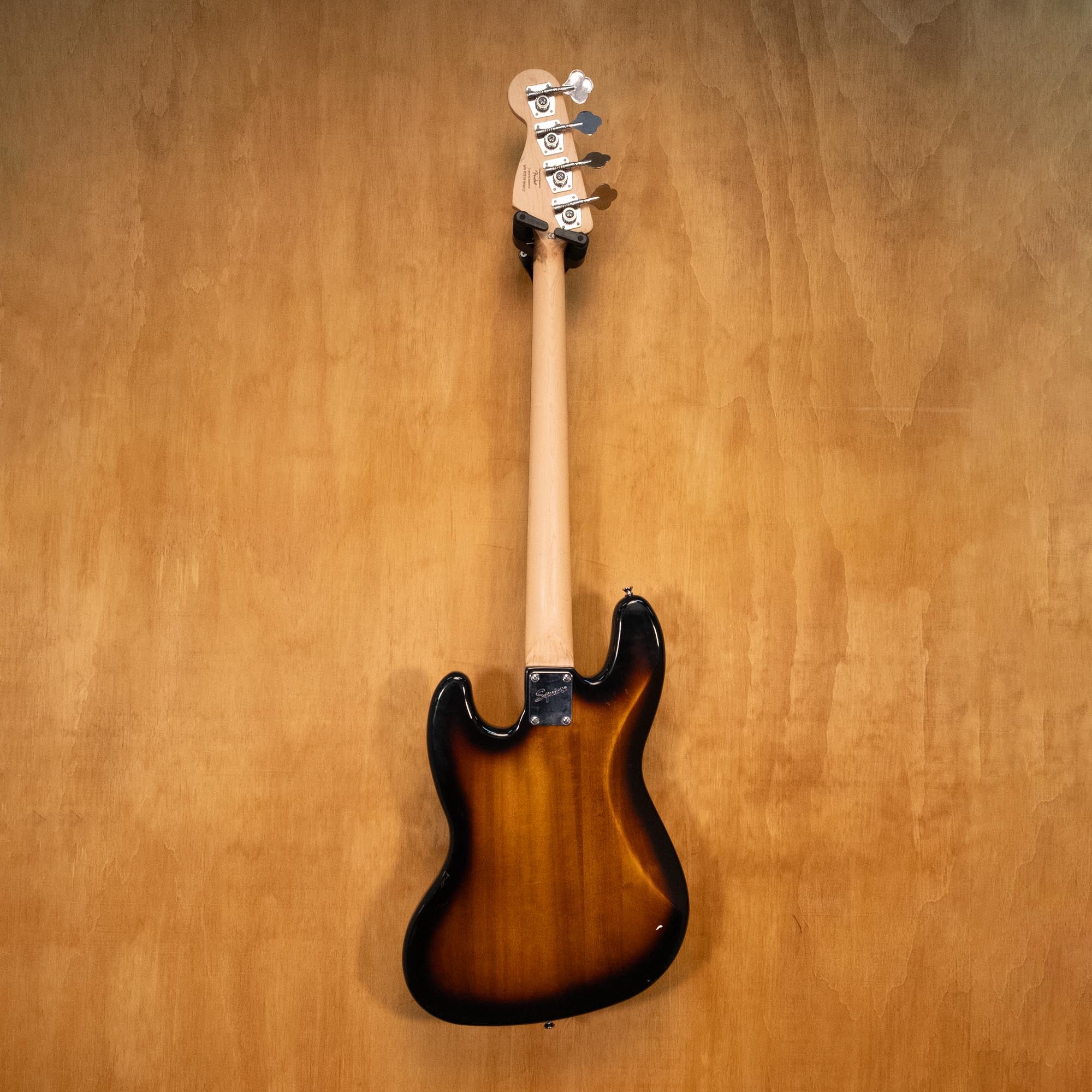 Squier Affinity Jazz Bass guitar in sunburst finish with maple neck and black pickguard, displayed on a stand.