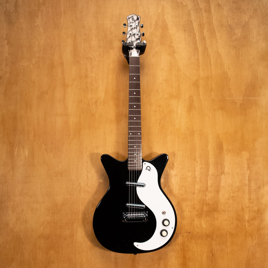Danelectro '59M NOS electric guitar in black with vintage-style body and chrome hardware, displayed on a stand.