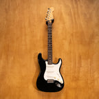 Fender Japan Standard Stratocaster electric guitar in black with white pickguard, displayed on a stand.