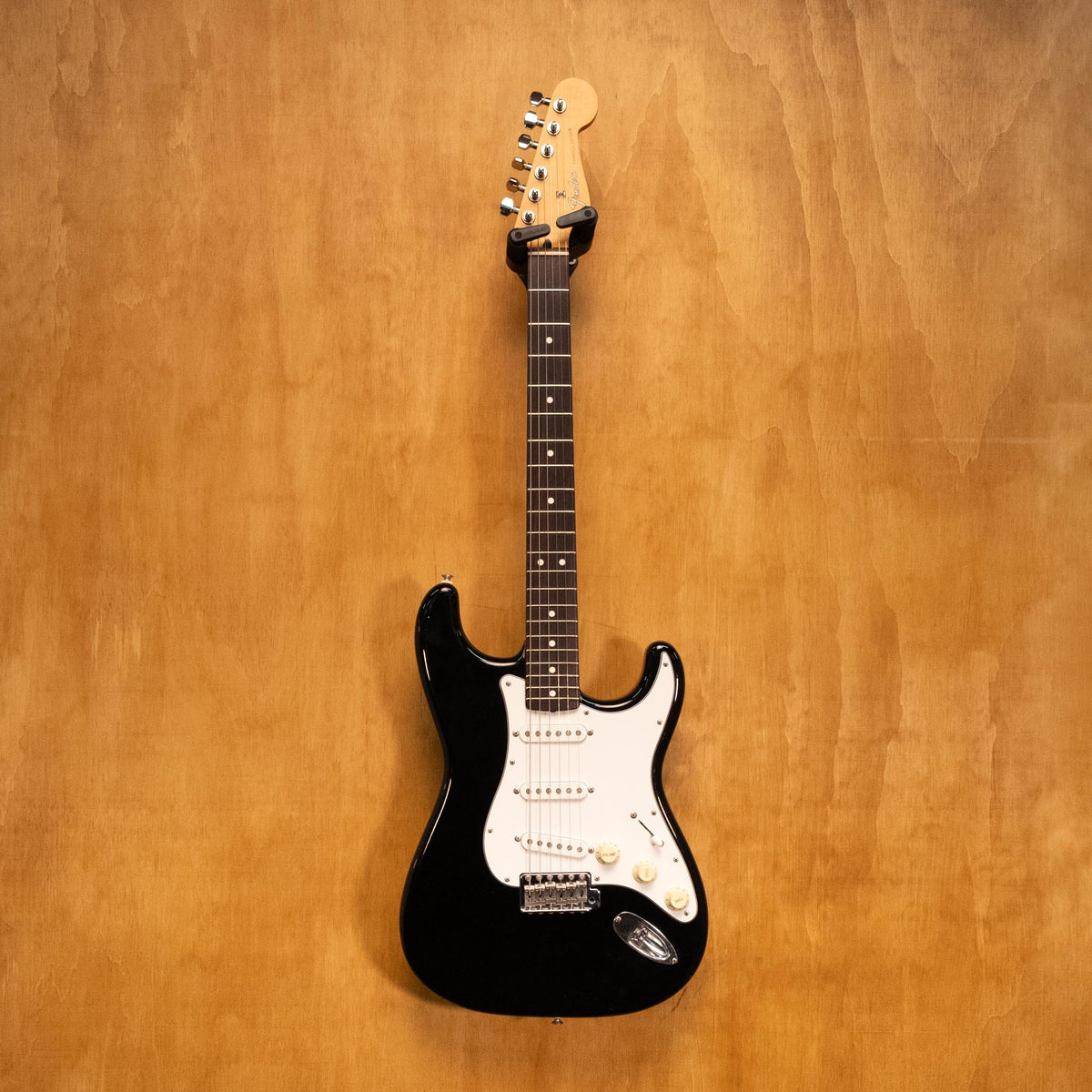 Fender Japan Standard Stratocaster electric guitar in black with white pickguard, displayed on a stand.