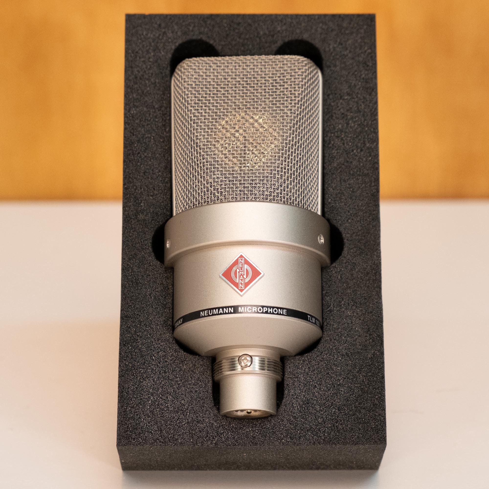 Neumann TLM103 cardioid condenser studio microphone with nickel finish, shown on a stand, ideal for professional recording setups.