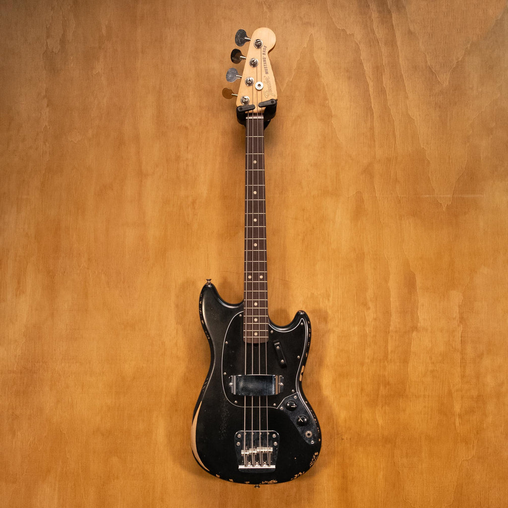 Fender JMJ Road Worn Mustang Bass Guitar in black with aged finish and vintage-style hardware, shown on a stand.