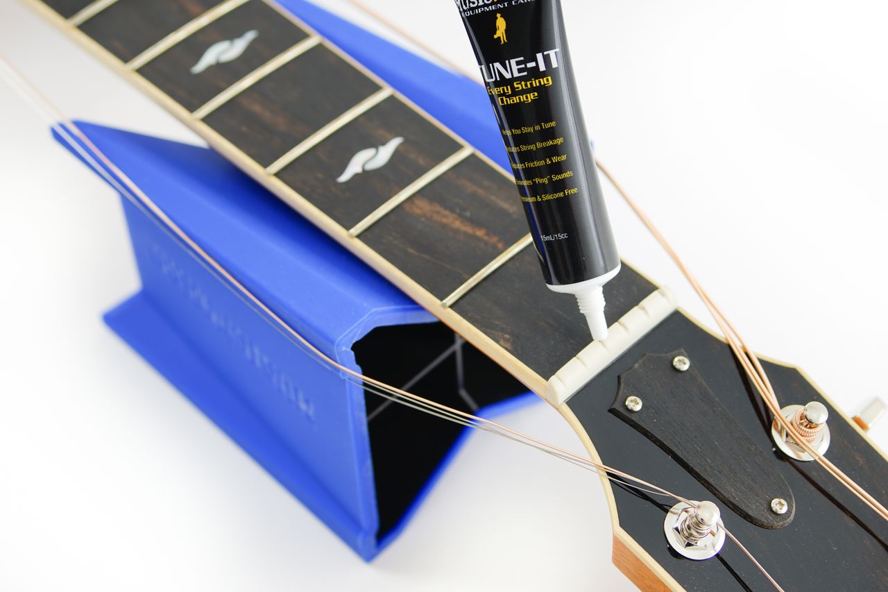Music Nomad MN106 Tune It Lubricant for guitar tuning pegs and bridges, in a small bottle with a white cap.