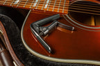 Jim Dunlop Trigger Fly Capo in gunmetal, a guitar capo with a sleek design, mounted on a guitar neck for quick, easy string tension adjustments.