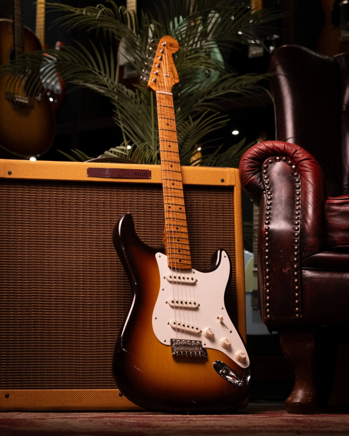 Electric guitar leaning against a amplifier with a leather chair in the background